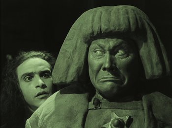 Movie still from “The Golem” (1920), directed by Paul Wegener – A man standing next to a statue of a person; Medium shot, Low angle