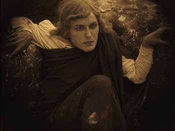 Movie still from “The Golem” (1920), directed by Paul Wegener – A woman sitting on the ground with her hands on her hips; Medium shot, High angle