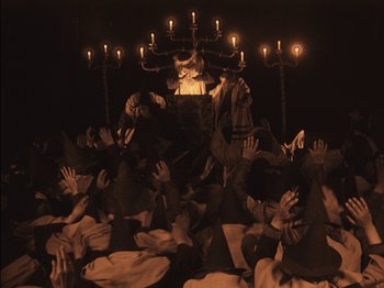 Movie still from “The Golem” (1920), directed by Paul Wegener – A group of people are gathered around a candelabrum; Wide shot, High angle
