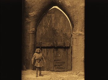Movie still from “The Golem” (1920), directed by Paul Wegener – A person standing in front of an arched doorway; Wide shot, Low angle