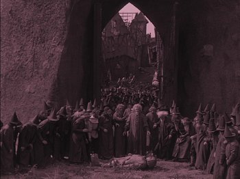 Movie still from “The Golem” (1920), directed by Paul Wegener – A group of people dressed as the wizards gathered in a cave; Wide shot, High angle
