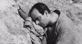 Movie still from “The Gospel According to St. Matthew” (1964), directed by Pier Paolo Pasolini – A black and white photo of a man laying on the ground; Medium shot, High angle