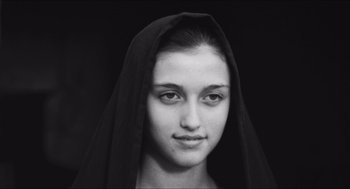 Movie still from “The Gospel According to St. Matthew” (1964), directed by Pier Paolo Pasolini – A young woman wearing a black headscarf and looking at the camera; Close Up shot, Low angle