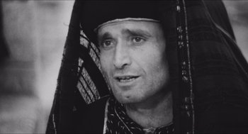 Movie still from “The Gospel According to St. Matthew” (1964), directed by Pier Paolo Pasolini – A black and white photo of a man wearing a headdress; Close Up shot, Over the shoulder angle