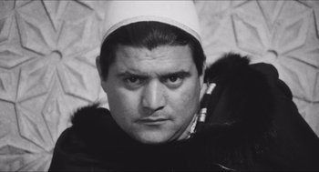 Movie still from “The Gospel According to St. Matthew” (1964), directed by Pier Paolo Pasolini – A black and white photo of a man wearing a hat; Close Up shot, Low angle