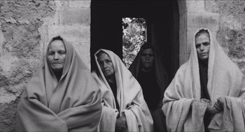 Movie still from “The Gospel According to St. Matthew” (1964), directed by Pier Paolo Pasolini – A group of people standing next to each other wearing blankets; Wide shot, High angle
