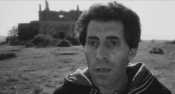 Movie still from “The Gospel According to St. Matthew” (1964), directed by Pier Paolo Pasolini – Black and white photograph of a man in front of an abandoned building; Close Up shot, Low angle