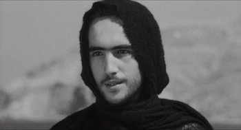 Movie still from “The Gospel According to St. Matthew” (1964), directed by Pier Paolo Pasolini – A black and white photo of a man wearing a hood; Close Up shot, Low angle