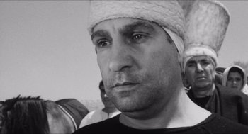 Movie still from “The Gospel According to St. Matthew” (1964), directed by Pier Paolo Pasolini – A black and white photo of a man with a bandage on his head; Close Up shot, Low angle