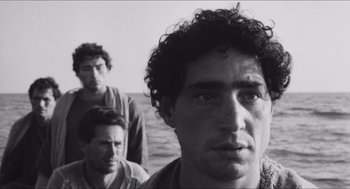 Movie still from “The Gospel According to St. Matthew” (1964), directed by Pier Paolo Pasolini – A black - and - white photo of three men standing next to each other; Close Up shot, Low angle