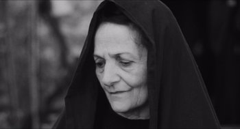 Movie still from “The Gospel According to St. Matthew” (1964), directed by Pier Paolo Pasolini – An older woman wearing a black veil and looking down; Close Up shot, Over the shoulder angle