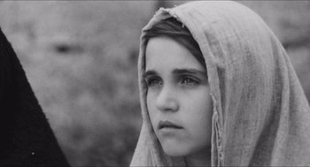 Movie still from “The Gospel According to St. Matthew” (1964), directed by Pier Paolo Pasolini – A young girl wearing a blanket and looking at the camera; Close Up shot, High angle