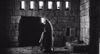 Movie still from “The Gospel According to St. Matthew” (1964), directed by Pier Paolo Pasolini – A person sitting in front of a stone wall; Extreme Wide shot, Low angle