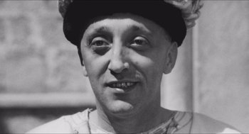 Movie still from “The Gospel According to St. Matthew” (1964), directed by Pier Paolo Pasolini – An old black and white photo of a man wearing a hat; Close Up shot, High angle