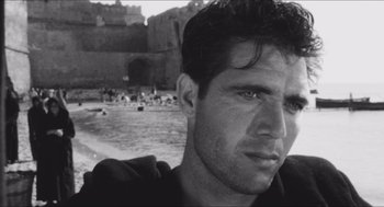 Movie still from “The Gospel According to St. Matthew” (1964), directed by Pier Paolo Pasolini – Black and white photograph of a man in front of a castle; Close Up shot, Low angle