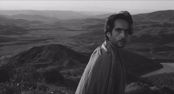Movie still from “The Gospel According to St. Matthew” (1964), directed by Pier Paolo Pasolini – A black and white photo of a man standing on top of a hill; Close Up shot, Over the shoulder angle