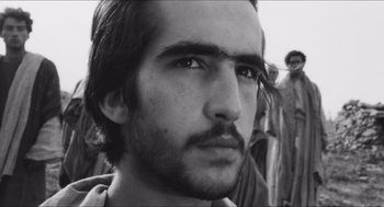 Movie still from “The Gospel According to St. Matthew” (1964), directed by Pier Paolo Pasolini – Black and white photograph of a young man looking at the camera; Close Up shot, Low angle