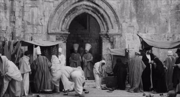 Movie still from “The Gospel According to St. Matthew” (1964), directed by Pier Paolo Pasolini – A black and white photo of a group of people in front of a building; Wide shot, High angle