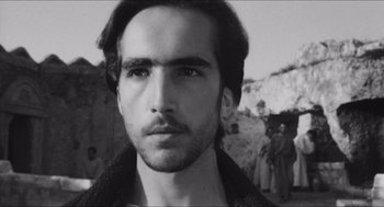 Movie still from “The Gospel According to St. Matthew” (1964), directed by Pier Paolo Pasolini – Black and white photograph of a young man in front of a group of people; Close Up shot, Low angle