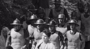 Movie still from “The Gospel According to St. Matthew” (1964), directed by Pier Paolo Pasolini – A black and white photo of a group of men in helmets; Wide shot, High angle