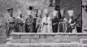 Movie still from “The Gospel According to St. Matthew” (1964), directed by Pier Paolo Pasolini – A black and white photo of a group of men wearing hats; Wide shot, High angle