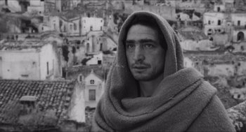 Movie still from “The Gospel According to St. Matthew” (1964), directed by Pier Paolo Pasolini – A black and white photo of a man with a towel around his neck; Close Up shot, Low angle