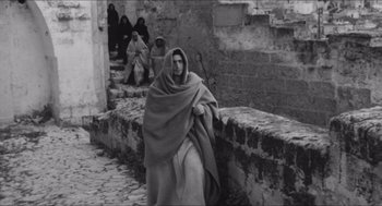 Movie still from “The Gospel According to St. Matthew” (1964), directed by Pier Paolo Pasolini – An old photo of a woman walking down the street; Wide shot, High angle
