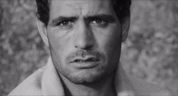 Movie still from “The Gospel According to St. Matthew” (1964), directed by Pier Paolo Pasolini – Black and white photograph of a man with a towel around his neck; Close Up shot, Over the shoulder angle