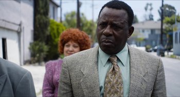 Movie still from “The Greasy Strangler” (2016), directed by Jim Hosking – A man in a suit standing next to a woman in an orange wig; Close Up shot, Over the shoulder angle