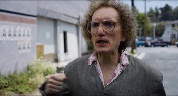Movie still from “The Greasy Strangler” (2016), directed by Jim Hosking – An older woman wearing glasses and a gray jacket; Close Up shot, Over the shoulder angle