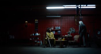 Movie still from “The Greasy Strangler” (2016), directed by Jim Hosking – A man sitting on a chair in a room; Wide shot, High angle