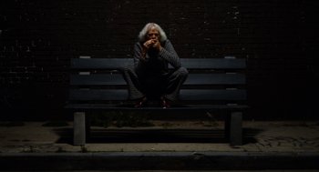 Movie still from “The Greasy Strangler” (2016), directed by Jim Hosking – A man sitting on top of a wooden park bench; Wide shot, Low angle