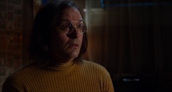 Movie still from “The Greasy Strangler” (2016), directed by Jim Hosking – An older woman wearing glasses and a yellow sweater; Close Up shot, Over the shoulder angle