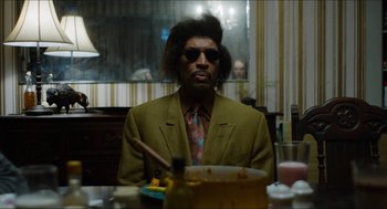 Movie still from “The Greasy Strangler” (2016), directed by Jim Hosking – A man sitting at a dinner table wearing a suit and tie; Medium shot, Over the shoulder angle
