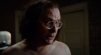 Movie still from “The Greasy Strangler” (2016), directed by Jim Hosking – A man with glasses is looking into the distance; Close Up shot, Over the shoulder angle
