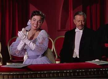 Movie still from “The Great Caruso” (1951), directed by Richard Thorpe – An older man and woman sitting in front of each other in front of a red curtain; Medium shot, Low angle