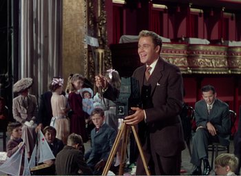 Movie still from “The Great Caruso” (1951), directed by Richard Thorpe – A man in a suit holding a camera in front of a group of people; Medium shot, Low angle