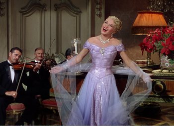 Movie still from “The Great Caruso” (1951), directed by Richard Thorpe – A woman in a purple dress is laughing while a man plays the violin; Medium shot, Low angle