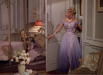 Movie still from “The Great Caruso” (1951), directed by Richard Thorpe – A woman in a purple dress standing in front of an open door; Wide shot, High angle