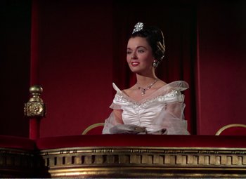 Movie still from “The Great Caruso” (1951), directed by Richard Thorpe – A woman in a white dress sitting at a table in front of a red curtain; Medium shot, Low angle