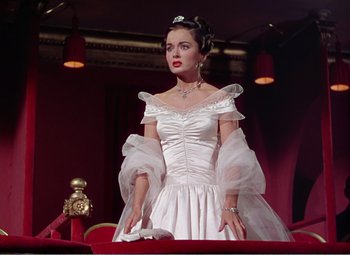 Movie still from “The Great Caruso” (1951), directed by Richard Thorpe – A woman in a white dress standing on a red couch; Medium shot, Low angle