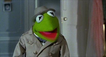 Movie still from “The Great Muppet Caper” (1981), directed by Jim Henson – A man dressed as kermit the frog wearing a trench coat and a hat; Close Up shot, Over the shoulder angle