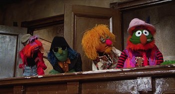 Movie still from “The Great Muppet Caper” (1981), directed by Jim Henson – A group of puppets sitting on top of a wooden stage; Wide shot, Low angle