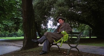 Movie still from “The Great Muppet Caper” (1981), directed by Jim Henson – A man sitting on a park bench with a kermit the frog toy; Wide shot, Low angle