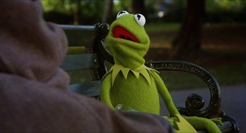 Movie still from “The Great Muppet Caper” (1981), directed by Jim Henson – A green stuffed animal sitting on top of a wooden bench; Close Up shot, Over the shoulder angle