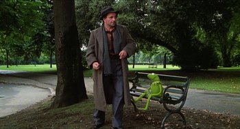 Movie still from “The Great Muppet Caper” (1981), directed by Jim Henson – A man walking in a park next to a bench; Wide shot, Low angle