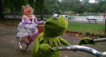 Movie still from “The Great Muppet Caper” (1981), directed by Jim Henson – Kermit the frog and miss piggy riding a bike in a park; Medium shot, Over the shoulder angle