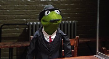 Movie still from “The Great Muppet Caper” (1981), directed by Jim Henson – A green frog wearing a black suit and hat; Medium shot, High angle