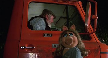Movie still from “The Great Muppet Caper” (1981), directed by Jim Henson – A man sitting in the driver's seat of an orange truck with a muppet in the passenger's seat; Close Up shot, High angle