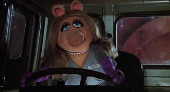 Movie still from “The Great Muppet Caper” (1981), directed by Jim Henson – A woman with long blonde hair sitting in the drivers seat of a bus; Close Up shot, High angle